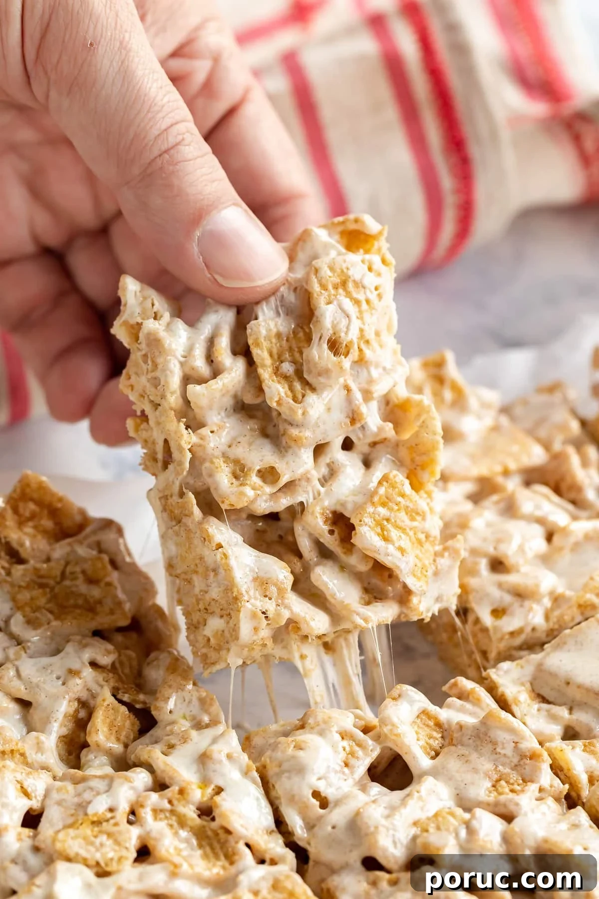 Homemade Cinnamon Toast Crunch Treat Bars Recipe 9 A hand pulling a freshly cut cereal bar from the rest of them with marshmallow stretching.