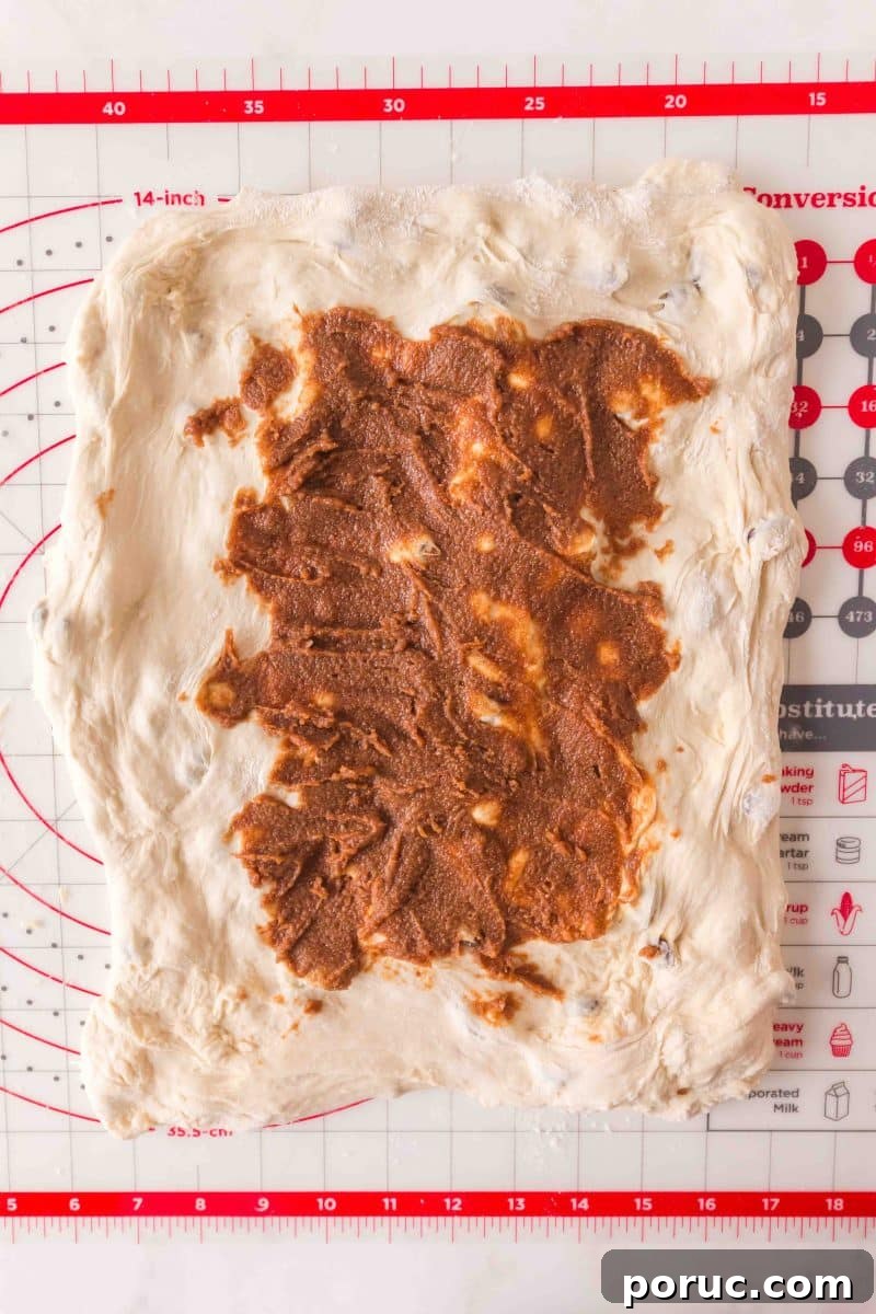 Sourdough Cinnamon Raisin Loaf — Soft, Sweet, Perfect Spice 11 Brown cinnamon butter mixture spread onto stretched rectangle of bread dough on floured surface. Hostess At Heart