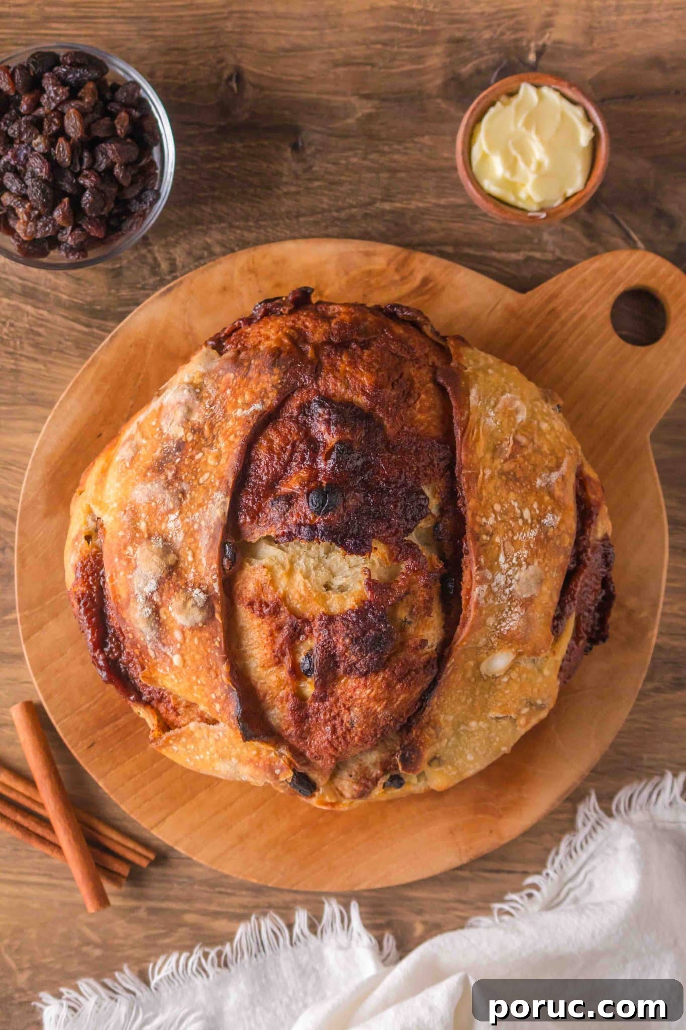 Sourdough Cinnamon Raisin Loaf — Soft, Sweet, Perfect Spice 15 Golden brown sourdough cinnamon raisin bread with visible raisins sitting on a cutting board. Hostess At Heart