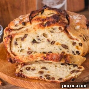 Sourdough Cinnamon Raisin Loaf — Soft, Sweet, Perfect Spice 19 Front view of a loaf of overnight sourdough cinnamon raisin bread sitting on a cutting board with the first two slices cut showing plump raisins and cinnamon swirls throughout a tender crumb. Hostess At Heart