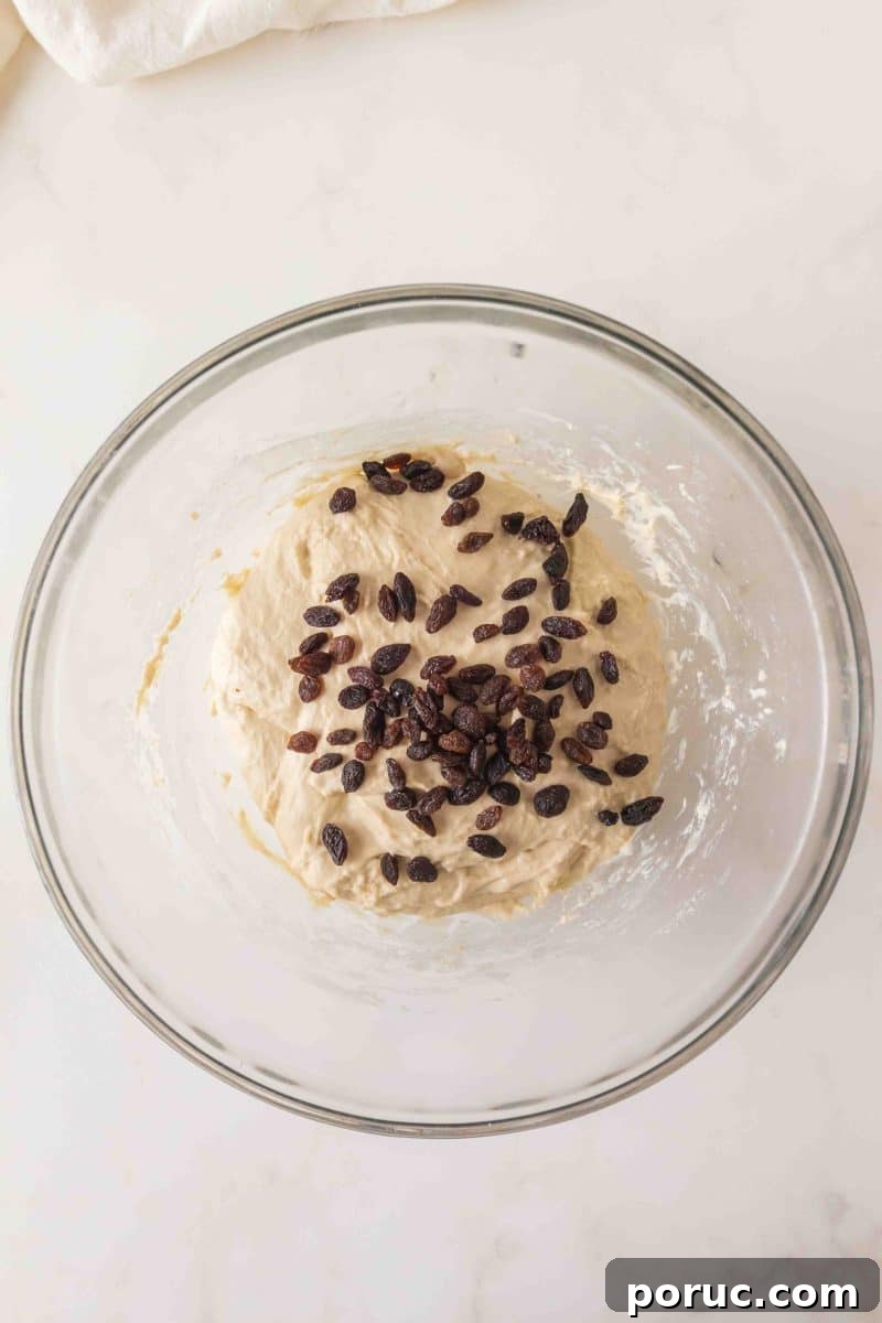 Sourdough Cinnamon Raisin Loaf — Soft, Sweet, Perfect Spice 7 Sticky sourdough bread dough in a mixing bowl with dark raisins on top ready for folding. Hostess At Heart