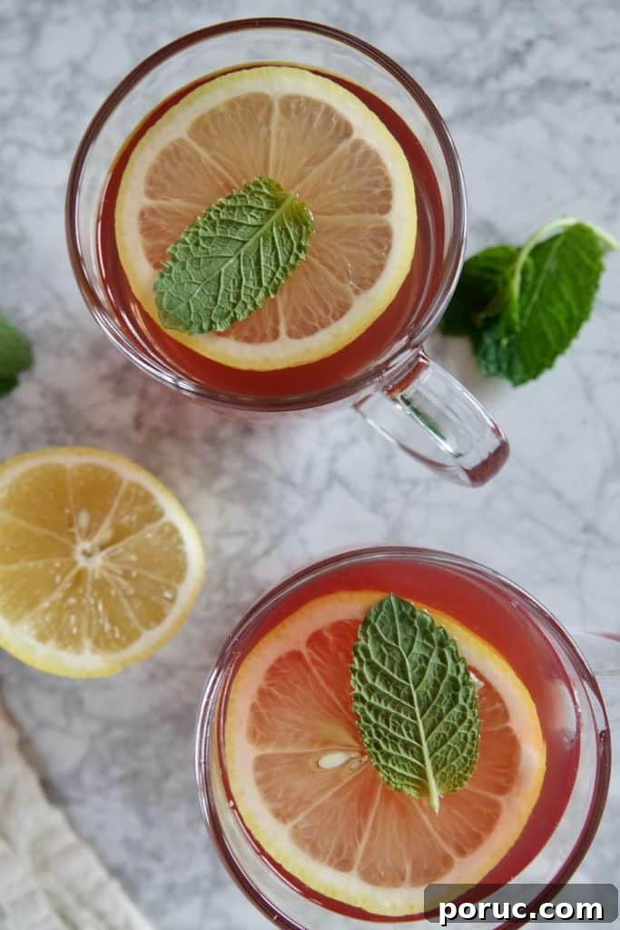 Honey Citrus Mint Tea — Copycat Starbucks Medicine Ball Recipe 2 View of two glass mugs with red tea, garnished with lemon slices and mint leaves.