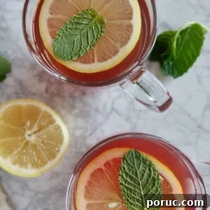Honey Citrus Mint Tea — Copycat Starbucks Medicine Ball Recipe 5 View of two glass mugs with red tea, garnished with lemon slices and mint leaves.