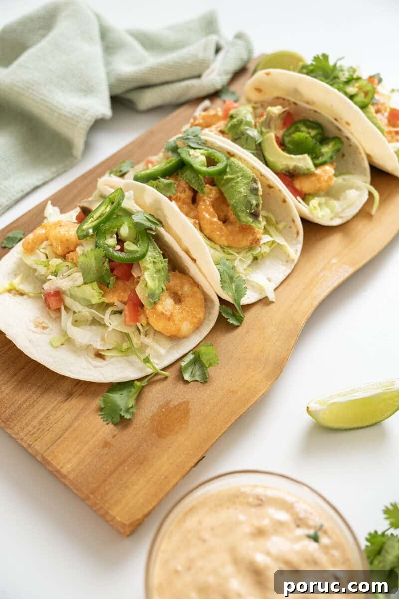 Volcano Shrimp Tacos: Spicy Grilled Shrimp with Lava Sauce 2 Volcano shrimp tacos on a cutting board topped with cilantro, tomatoes, jalapeno, and avocado.