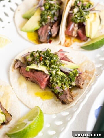 Chimichurri steak tacos on a plate with limes.