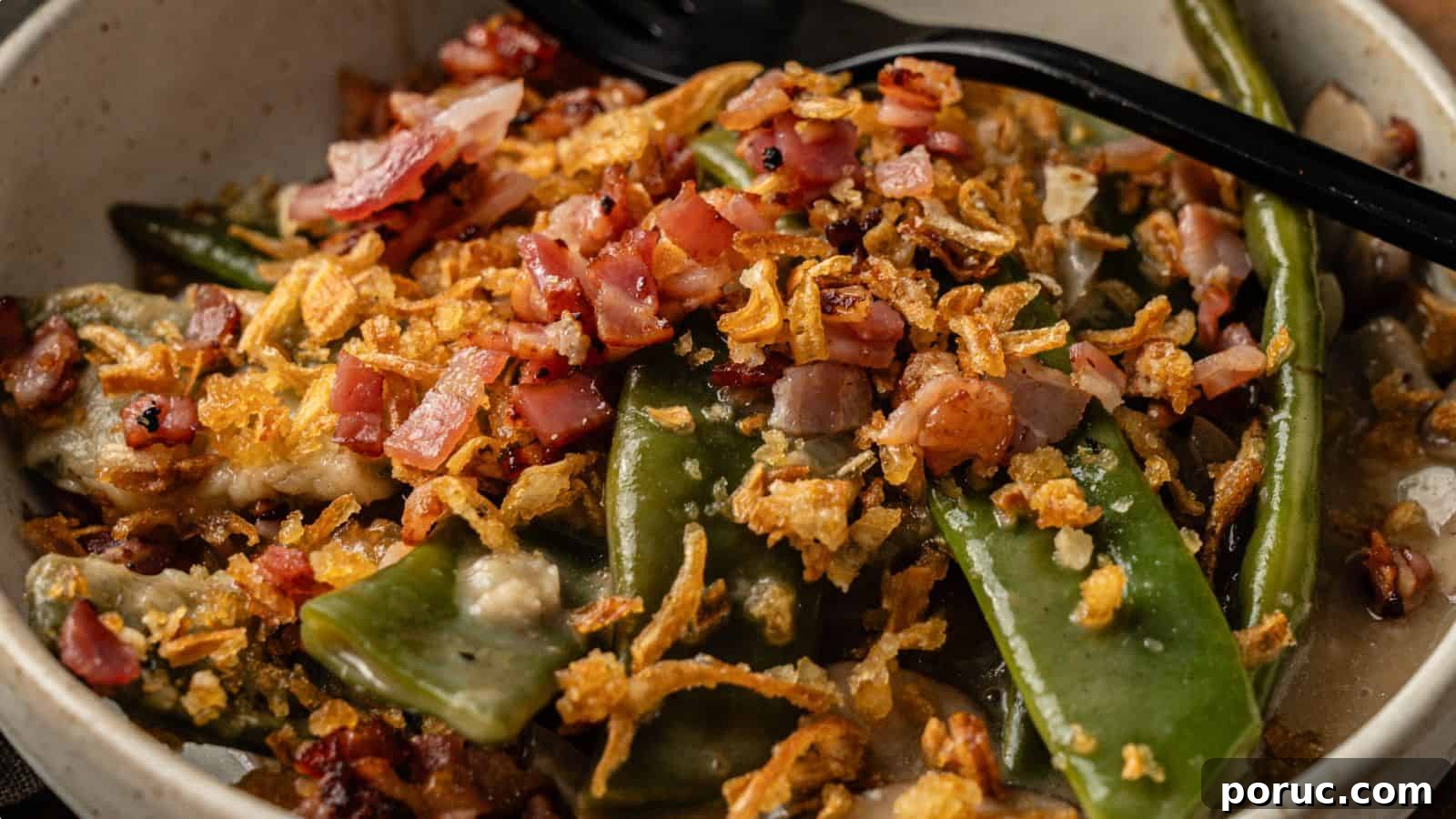 29 Air Fryer Casseroles Perfect for Busy Weeknight Dinners 13 A close-up of a dish with green beans, snap peas, chopped bacon, and crispy fried onions, served in a bowl with a black spoon.