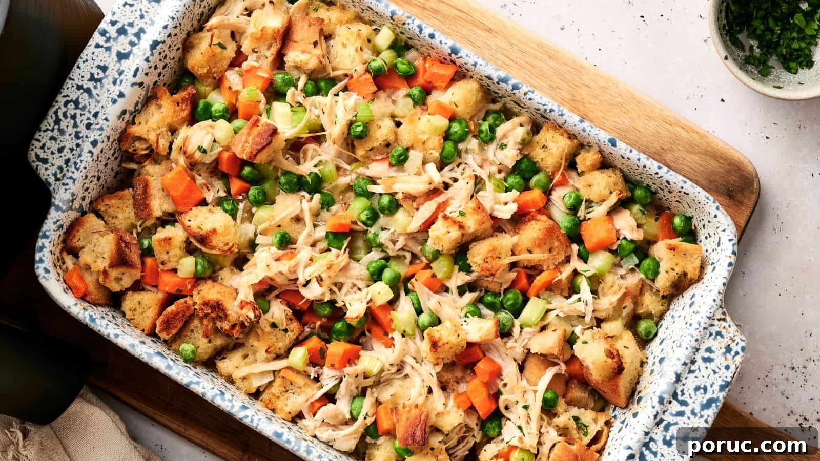 29 Air Fryer Casseroles Perfect for Busy Weeknight Dinners 22 A casserole dish filled with baked bread cubes, shredded chicken, peas, carrots, and celery, arranged on a wooden board.