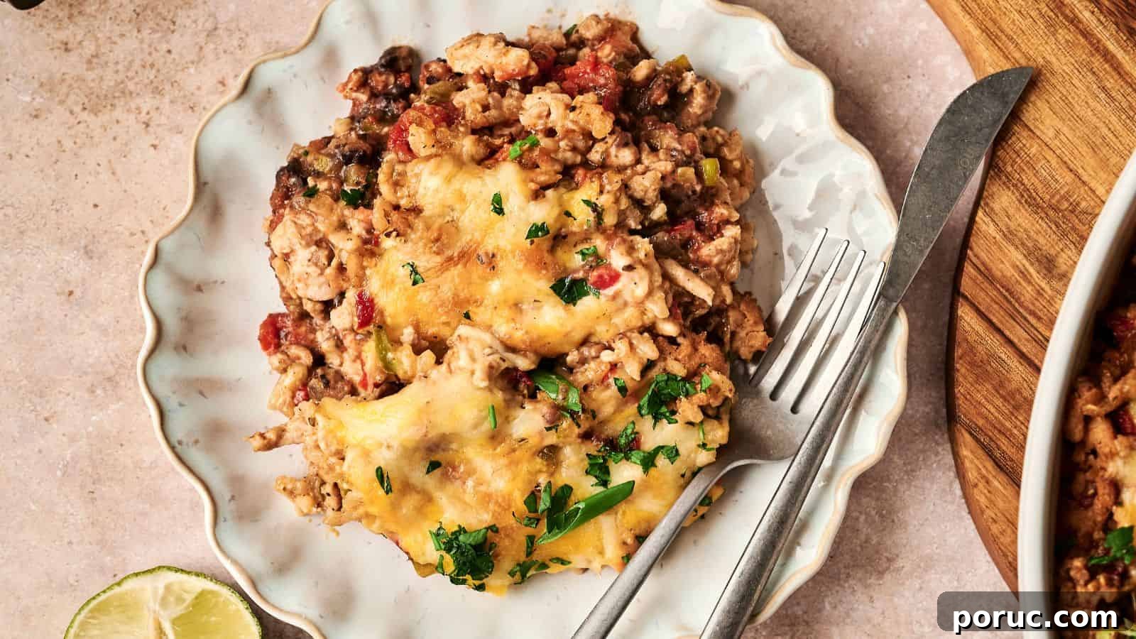29 Air Fryer Casseroles Perfect for Busy Weeknight Dinners 9 A plate with a serving of cheesy casserole containing ground meat, beans, and chopped herbs, accompanied by a fork and knife. A lime wedge is partially visible on the side.