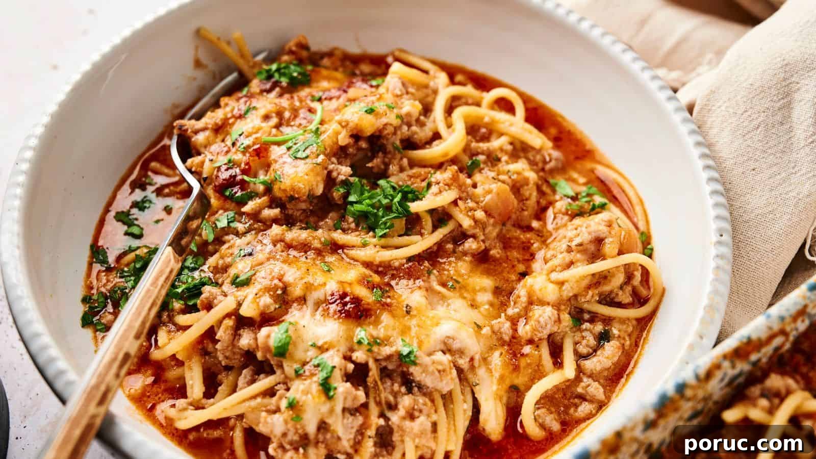29 Air Fryer Casseroles Perfect for Busy Weeknight Dinners 10 A bowl of spaghetti topped with meat sauce, melted cheese, and chopped parsley, with a fork resting inside.