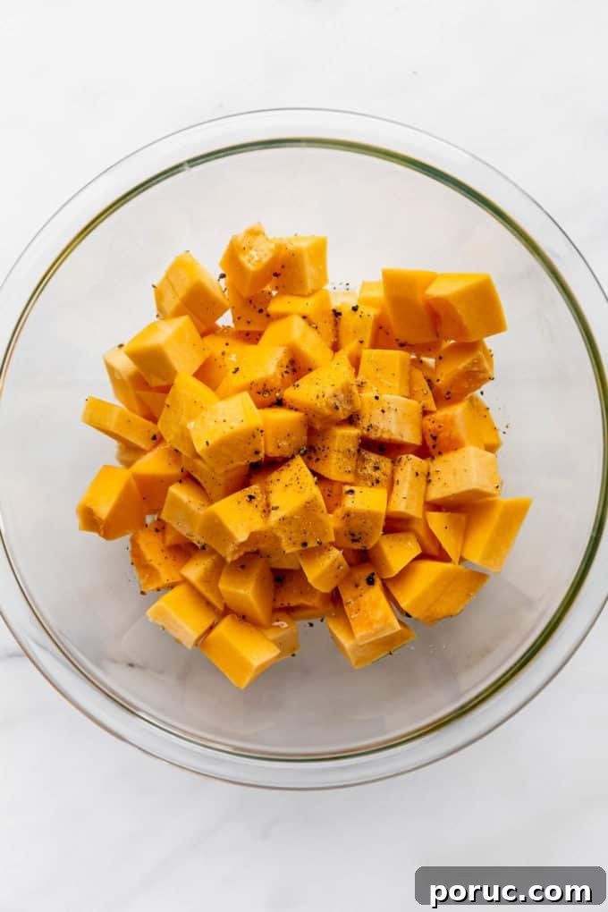Roasted Pumpkin Salad with Maple Vinaigrette and Toasted Seeds 5 A clear mixing bowl with cubes of pumpkin it it tossed in olive oil, salt and pepper