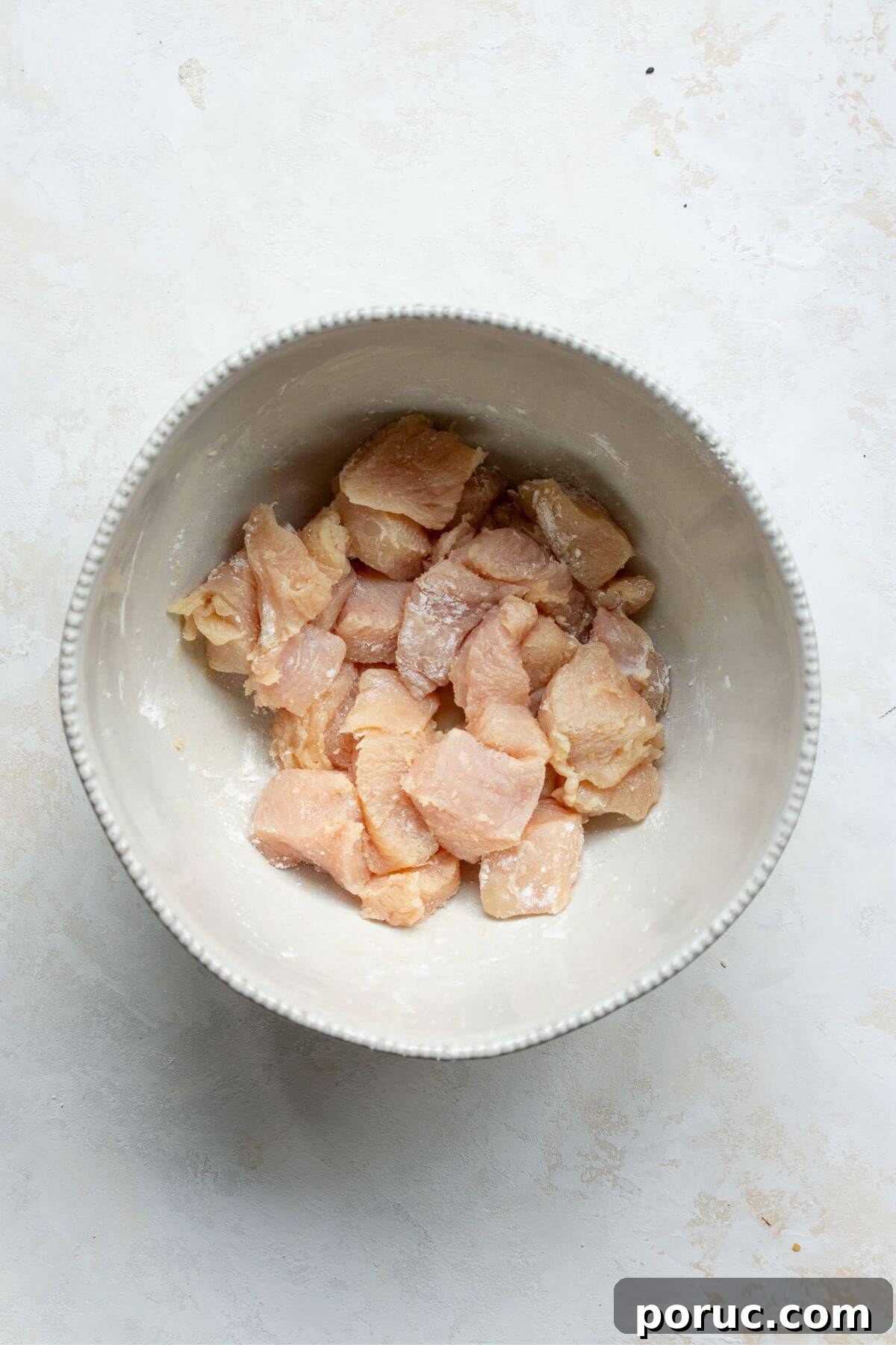 Crispy Air Fryer Orange Chicken Recipe You’ll Love 5 Chicken breast pieces in a mixing bowl with sesame oil and arrowroot powder.