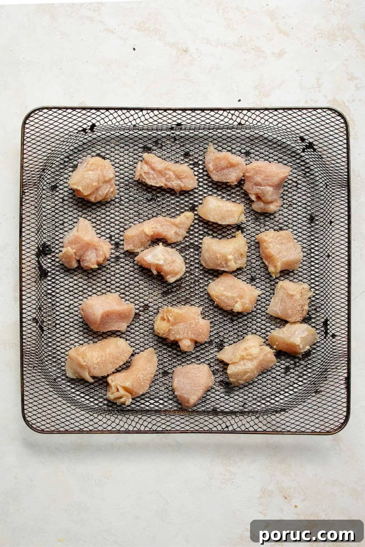 Crispy Air Fryer Orange Chicken Recipe You’ll Love 6 Coated raw chicken pieces spread out in an air fryer basket before cooking.