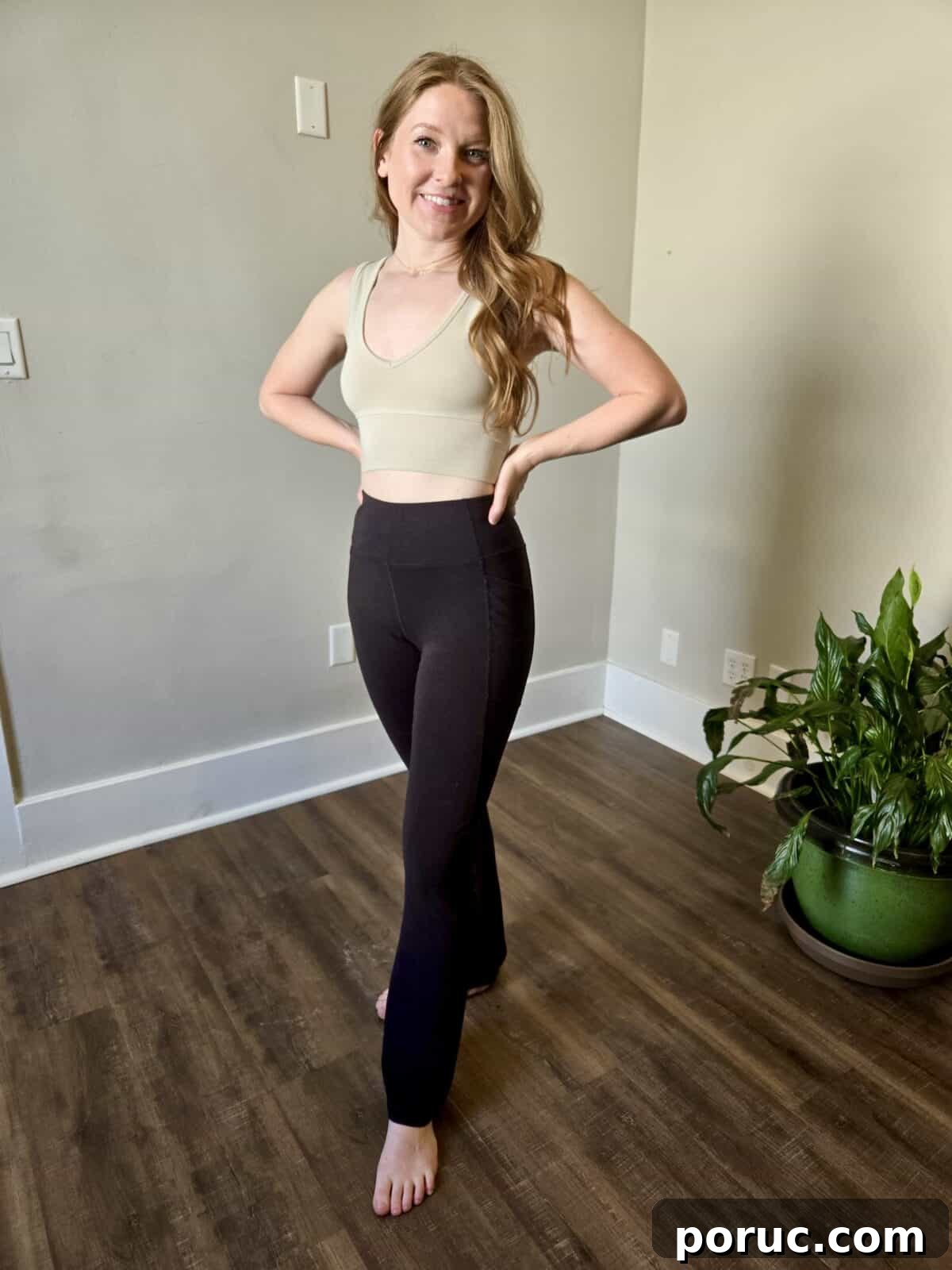 A woman posing in fitted tan cropped tank and black yoga pants from Happy Earth.