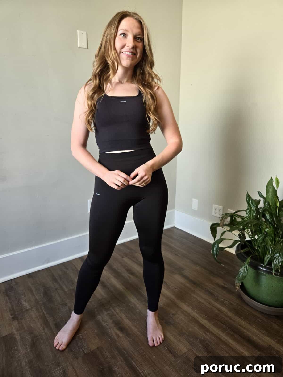 A smiling woman wearing a black fitted cropped tank top and high-waisted black leggings from Pangaia.