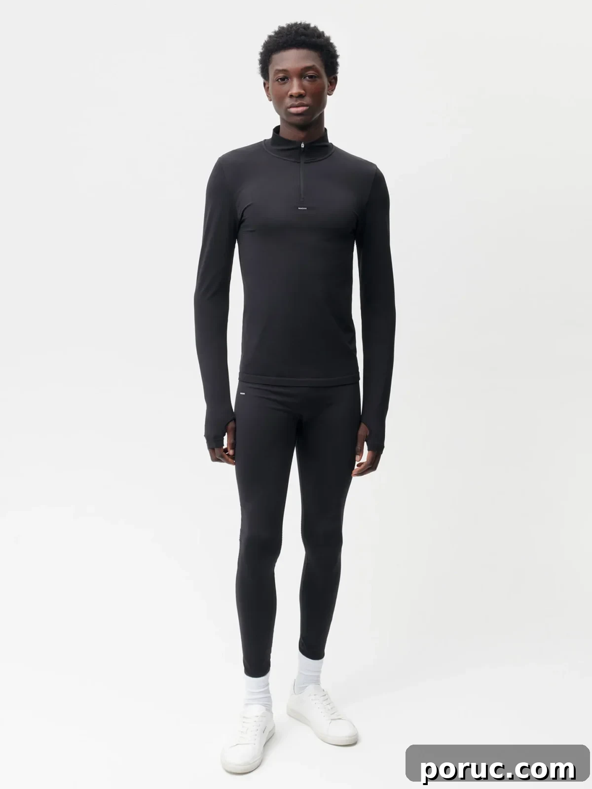 A model stands full-length in a black long-sleeved athletic top with a quarter-zip and thumbholes from Pangaia, paired with matching black leggings.
