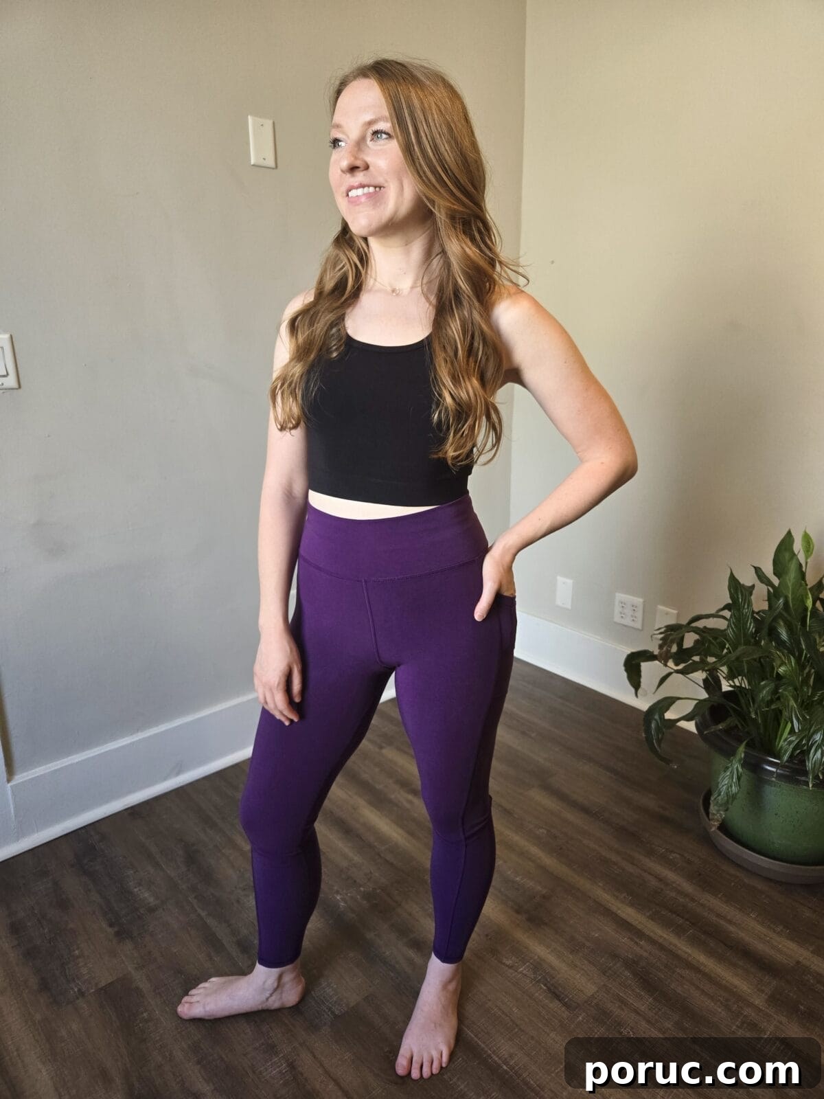 A barefoot woman posing in a black cropped tank top and high-waisted purple leggings with a side pocket from Reprise.