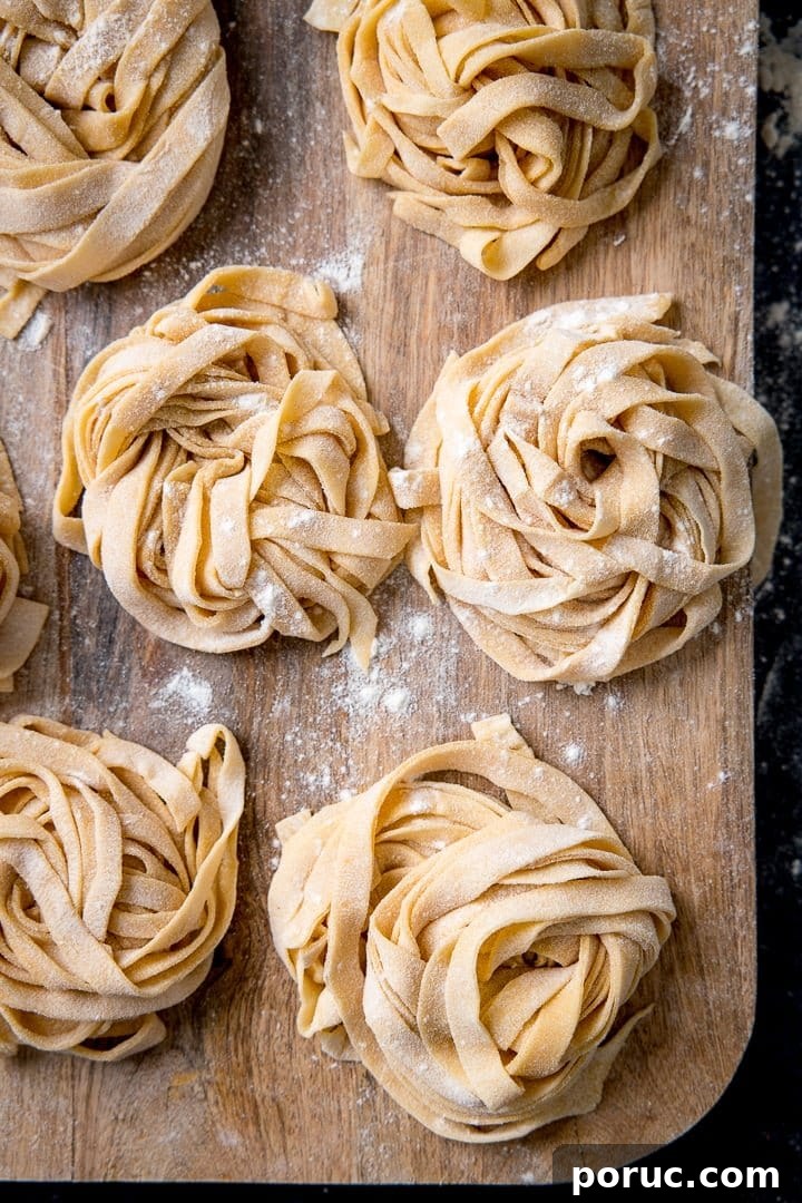 Piles of homemade pasta with flour sprinkled on, on wooden board