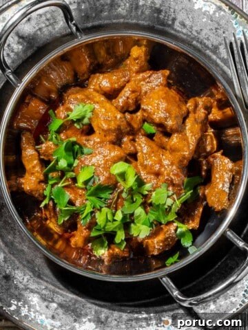 Aromatic beef curry with coconut milk in a balti bowl with a side of rice.