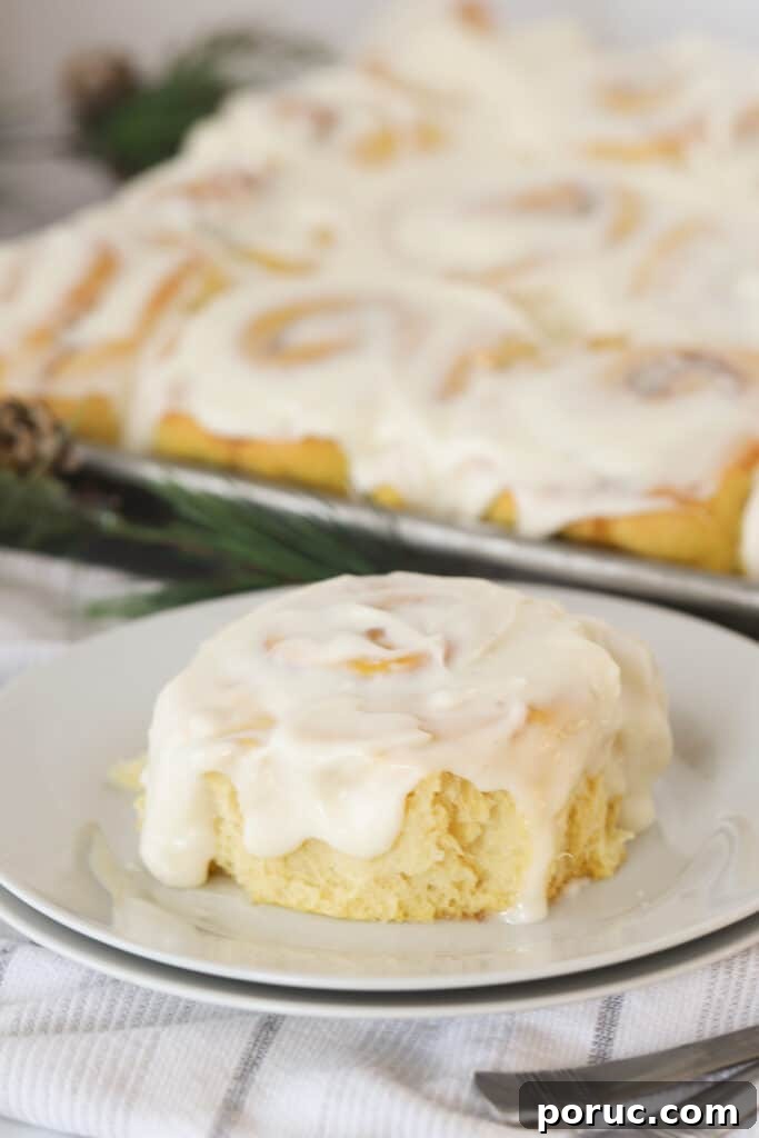 A white plate with a pumpkin cinnamon roll on it, topped with white frosting.
