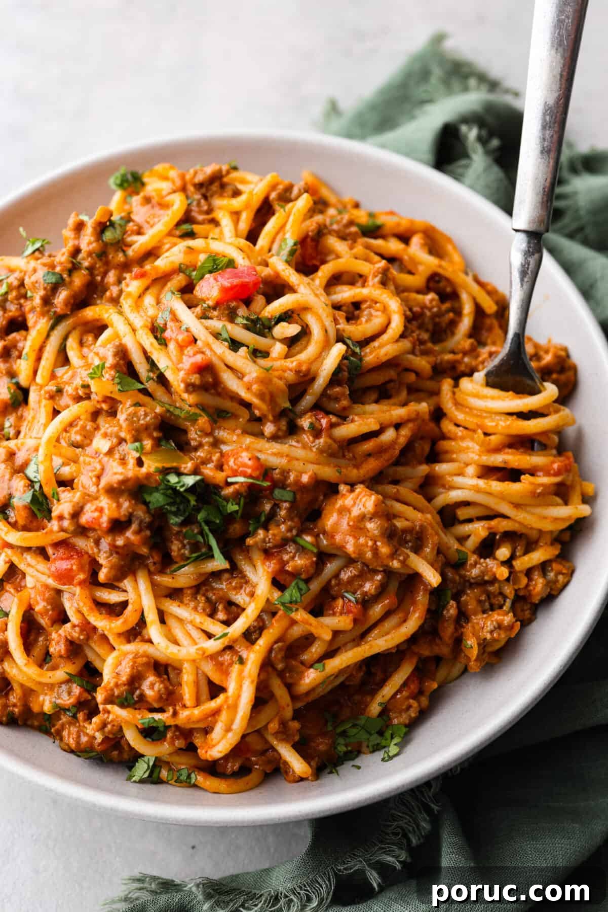 Taco spaghetti brings together two family favorites, tacos and pasta, in one cheesy, flavor packed dish! With taco-seasoned beef, melty cheese, and zesty tomatoes, it’s a weeknight win everyone will love. A serving of taco spaghetti, topped with fresh herbs.