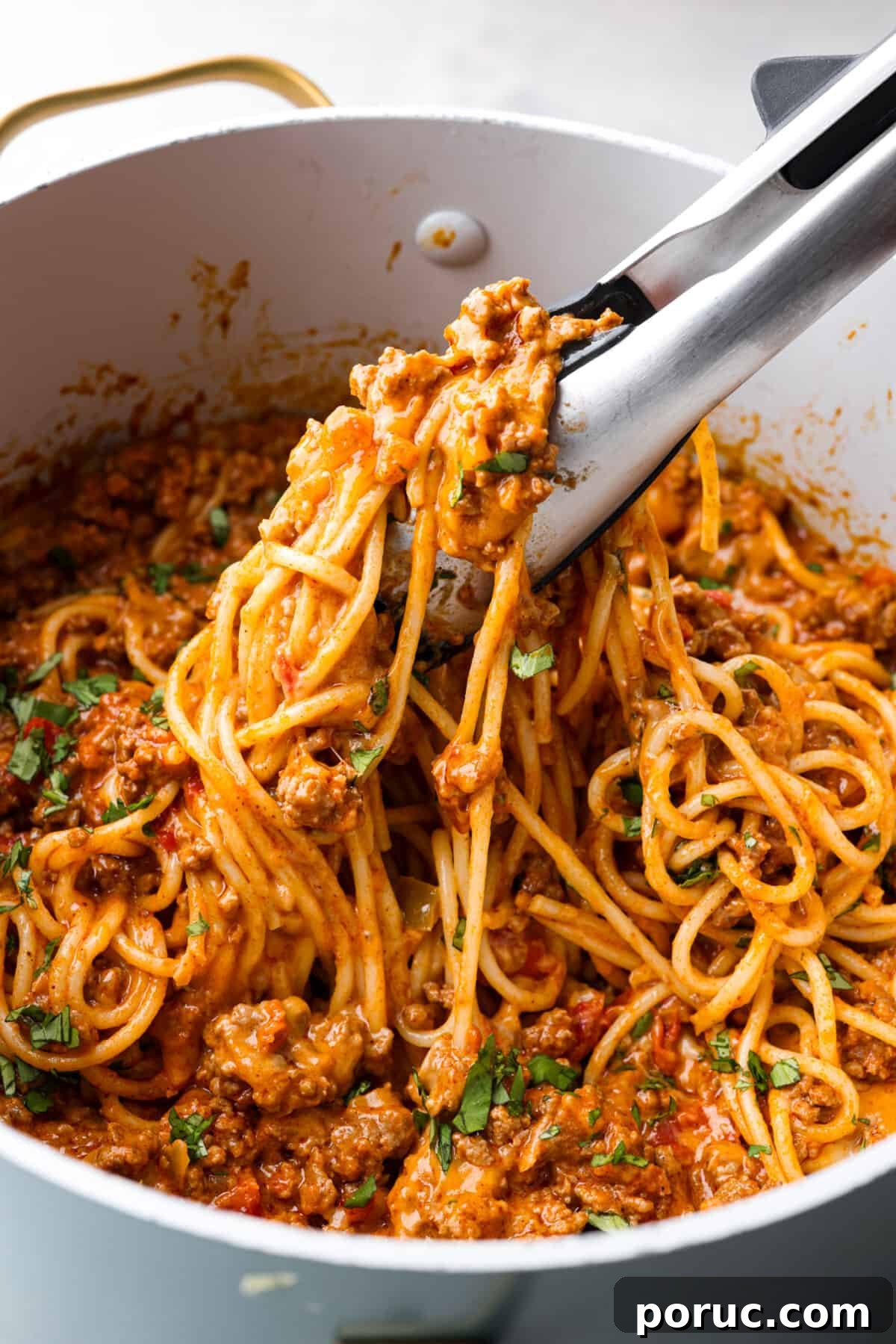 Taco spaghetti brings together two family favorites, tacos and pasta, in one cheesy, flavor packed dish! With taco-seasoned beef, melty cheese, and zesty tomatoes, it’s a weeknight win everyone will love. Taco spaghetti in a large pot, being picked up with tongs.