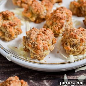 Cheesy Sausage Balls with 3 Ingredients: Quick Party Appetizer 12 The Bisquick sausage balls are on a white plate surrounded by shredded cheese.