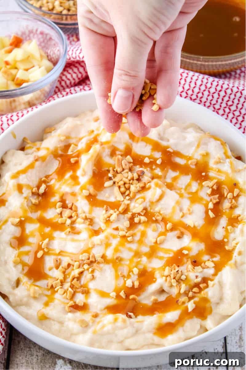 Get all the Fall feels with this 5-minute Caramel Apple Cheesecake Dip! Crazy easy to make and perfect for sharing! cheesecake dip with caramel drizzled on top and hand sprinkling on chopped nuts