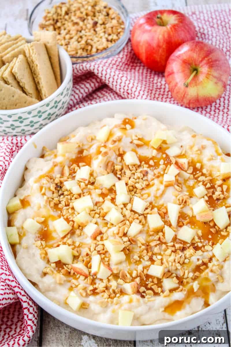 Get all the Fall feels with this 5-minute Caramel Apple Cheesecake Dip! Crazy easy to make and perfect for sharing! caramel apple cheesecake dip in a serving bowl next to graham crackers, chopped nuts, and gala apples
