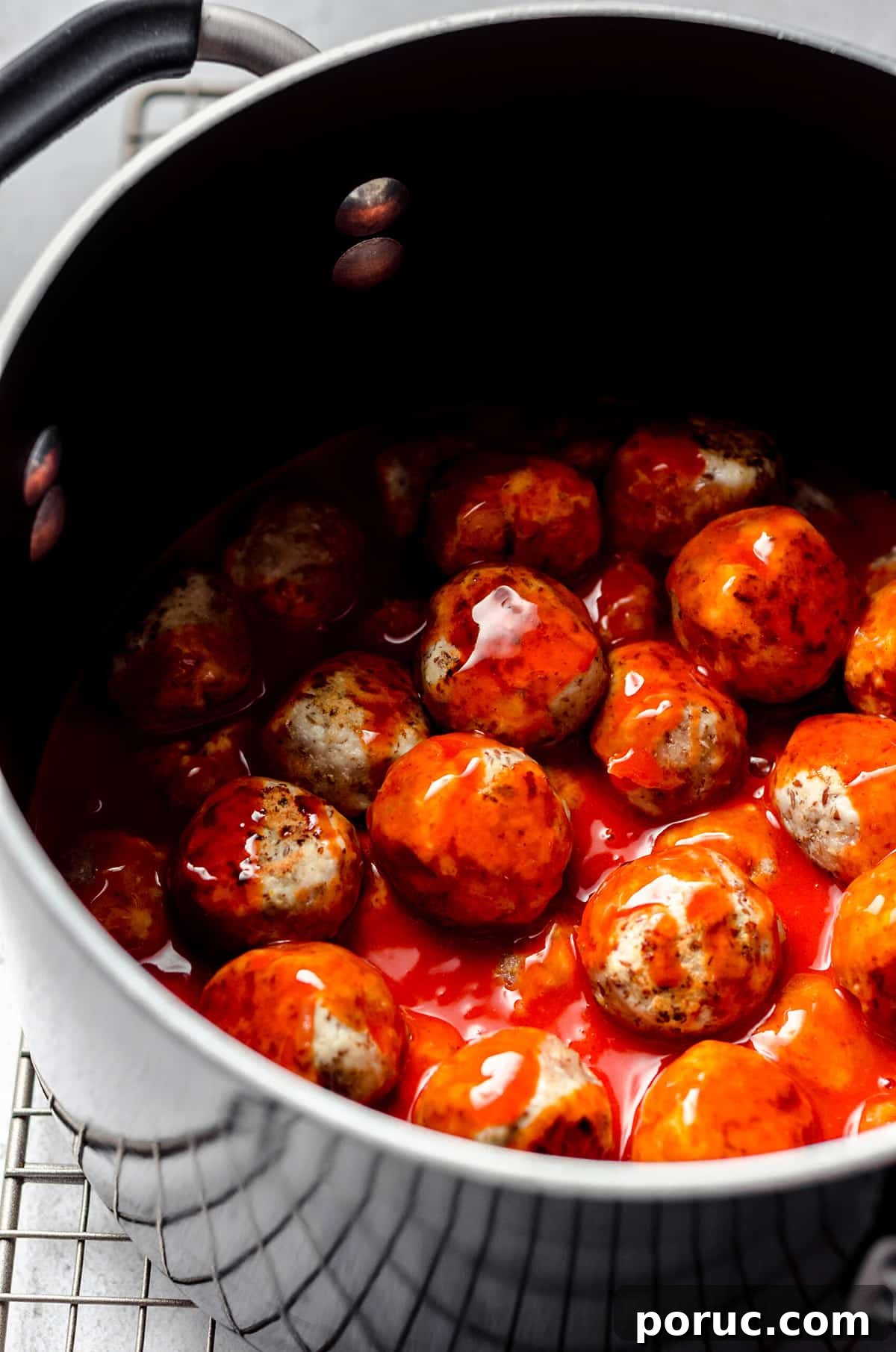 Meatballs tossed with buffalo sauce in a saucepan.