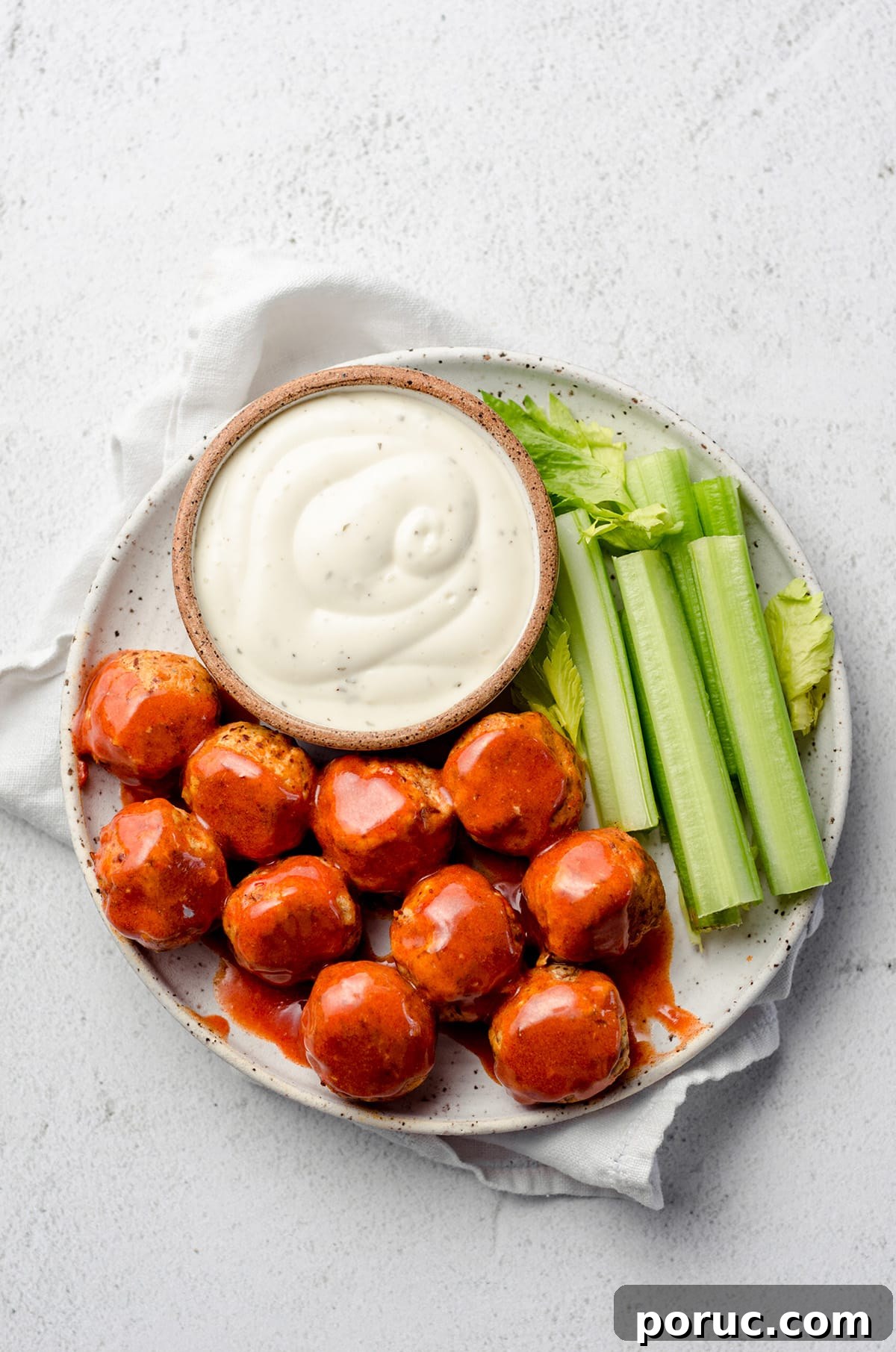 A plate with buffalo sauce coated meatballs, celery, and a creamy dressing.