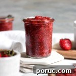 A glass jar of strawberry jam with fresh strawberries.