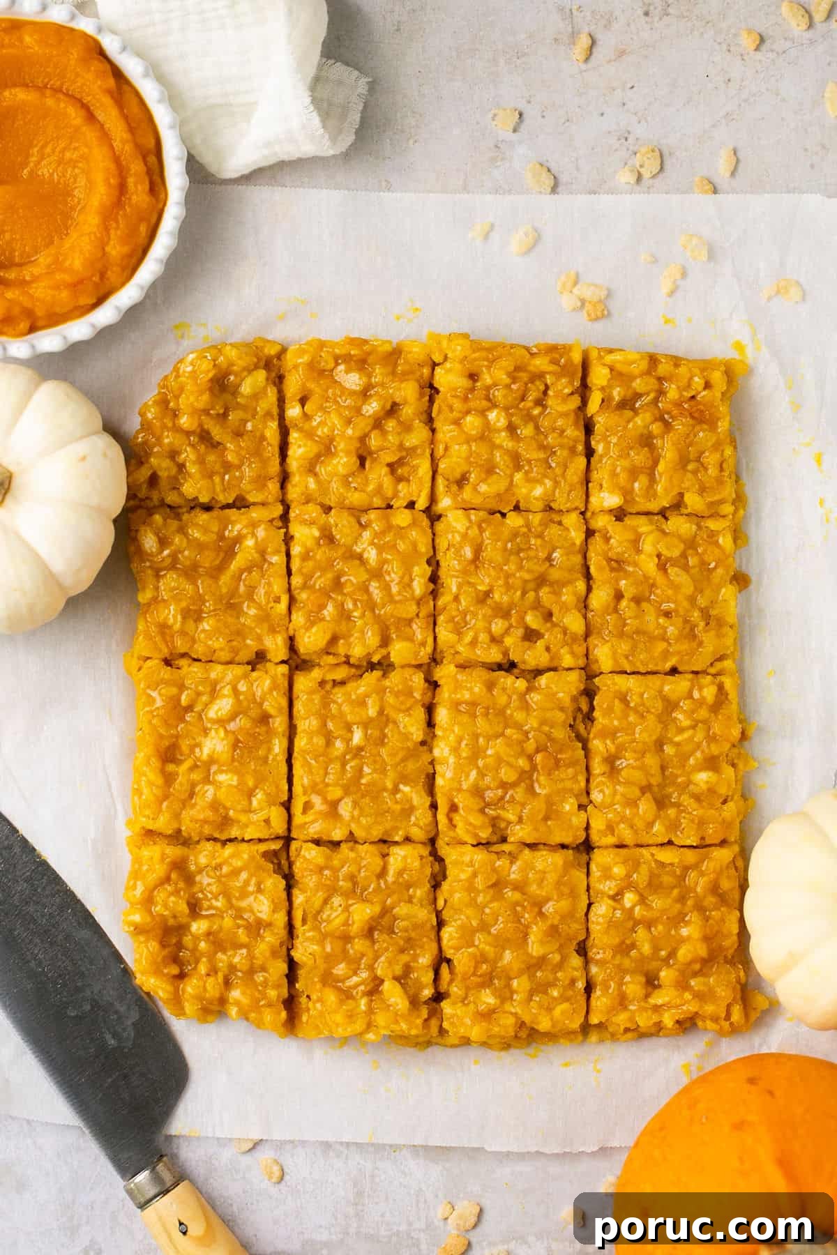 Pumpkin Marshmallow Rice Krispie Treats for Fall Parties 7 A batch of pumpkin Rice Krispie treats that have been cut into squares on a piece of parchment paper.