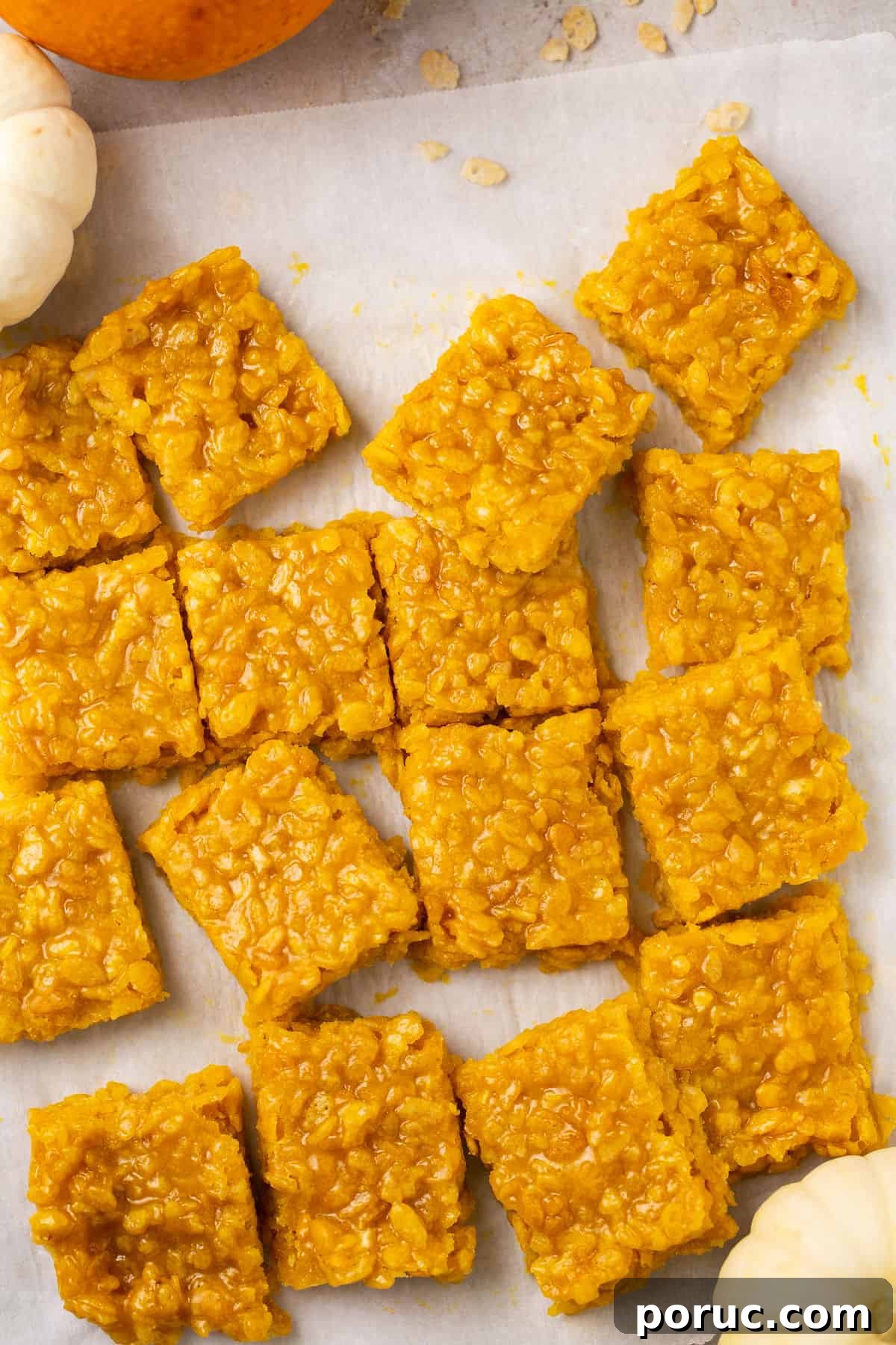 Pumpkin Marshmallow Rice Krispie Treats for Fall Parties 8 Cut up Rice Krispie squares on parchment paper with some cereal pieces around the squares.