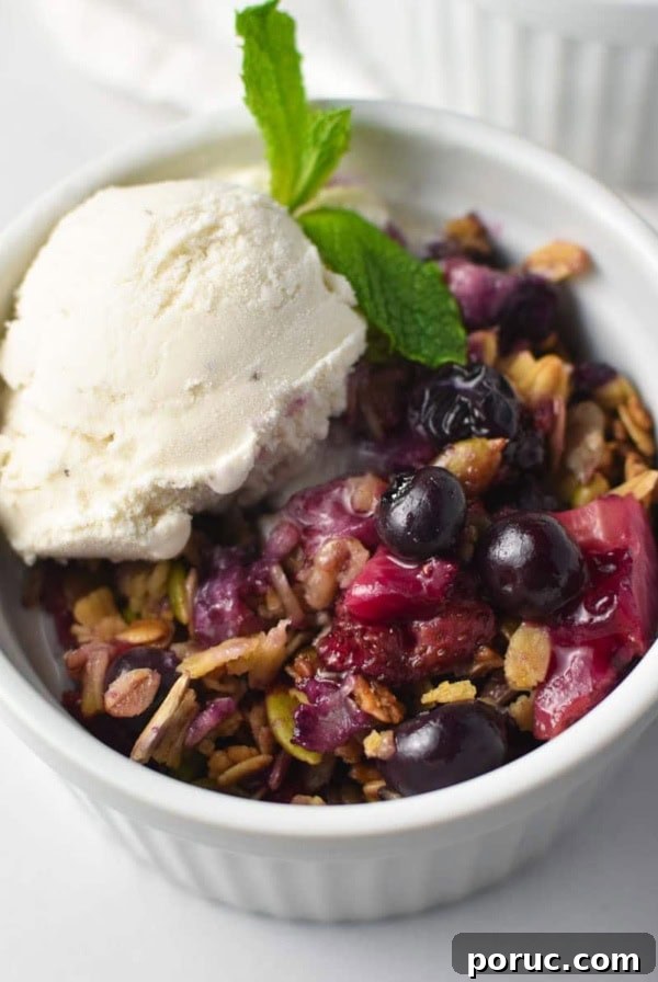 Crustless Blueberry Pie Recipe: Quick, Creamy Summer Dessert 13 A strawberry blueberry crisp topped with oats and vanilla ice cream with a sprig of mint in a white bowl