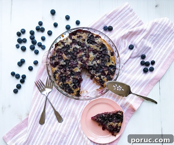 Crustless Blueberry Pie Recipe: Quick, Creamy Summer Dessert 17 A crustless blueberry pie with a slice cut out and utensils on a pink striped towel