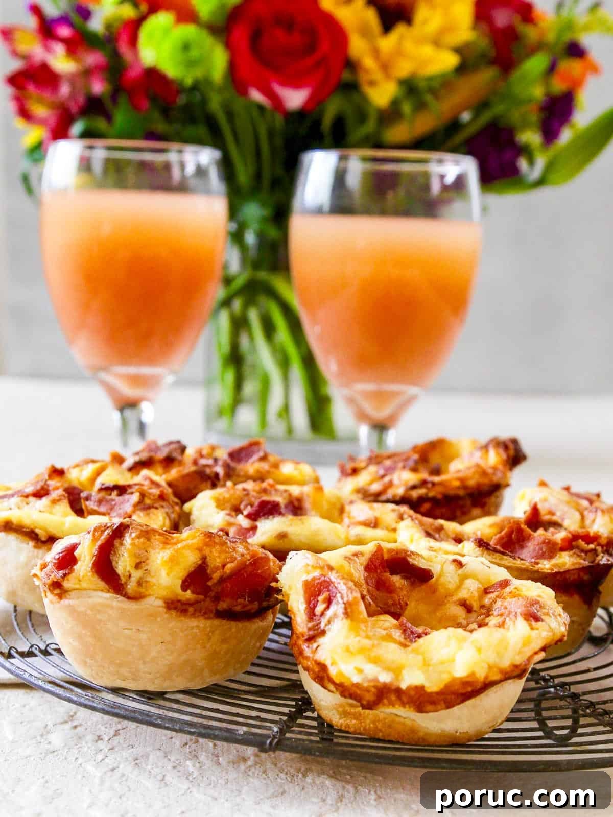 Bite-Sized Brie & Bacon Mini Quiches: Savory Party Appetizers 7 Two glasses of grapefruit juice with mini quiches and flowers in the background at brunch.