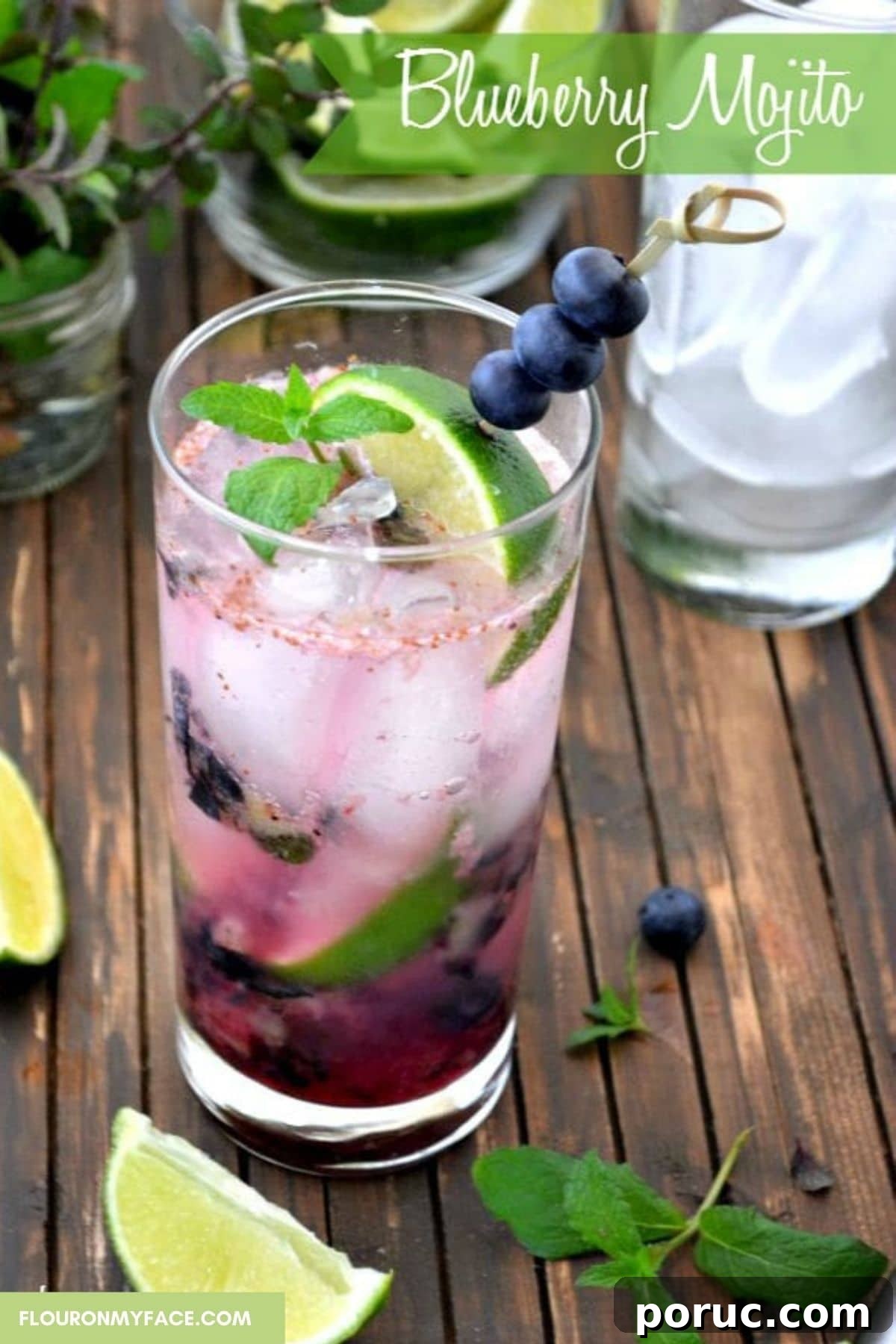 A tall glass filled with blueberry Mojito, lime wedges and a glass in the background.