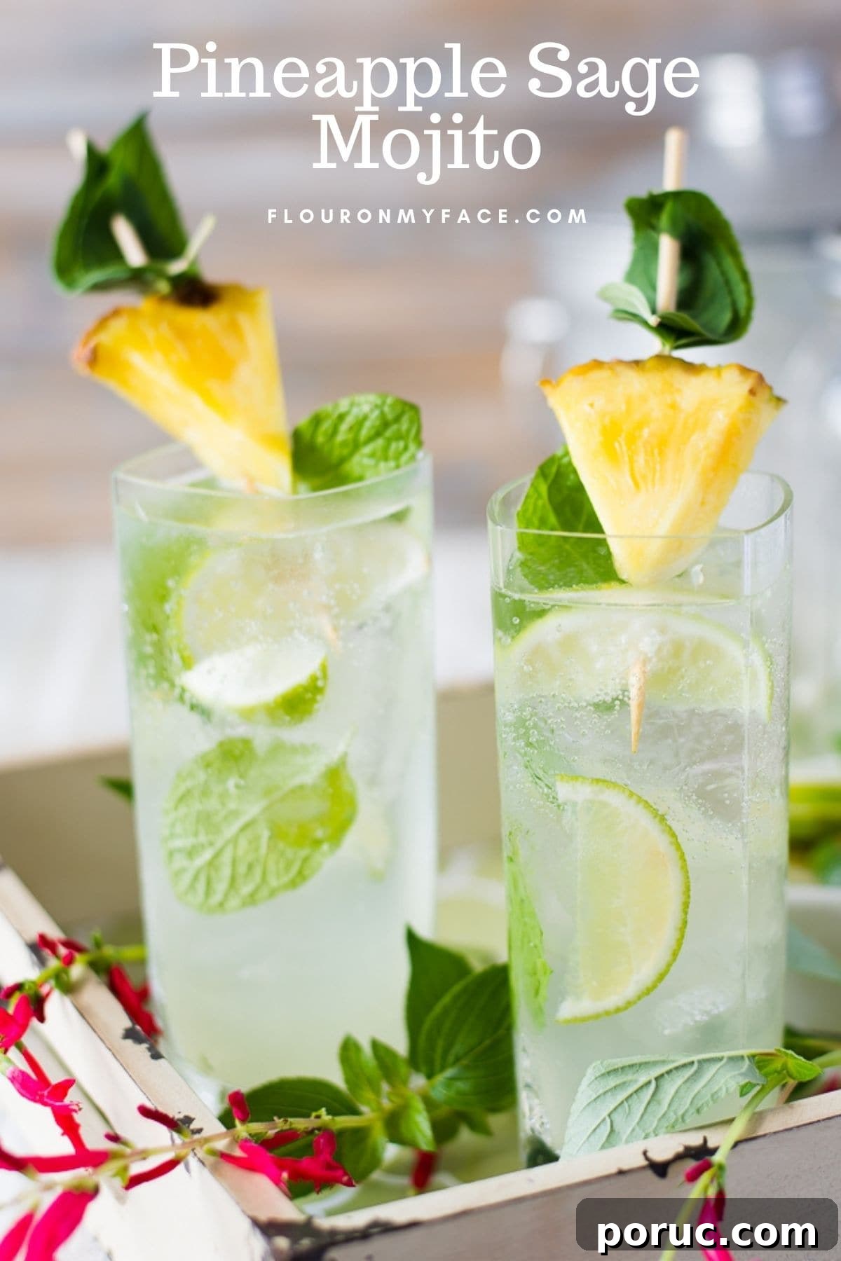 Two tall glasses on a serving tray filled with Pineapple Sage Mojito, garnished with pineapple wedges and mint leaves.