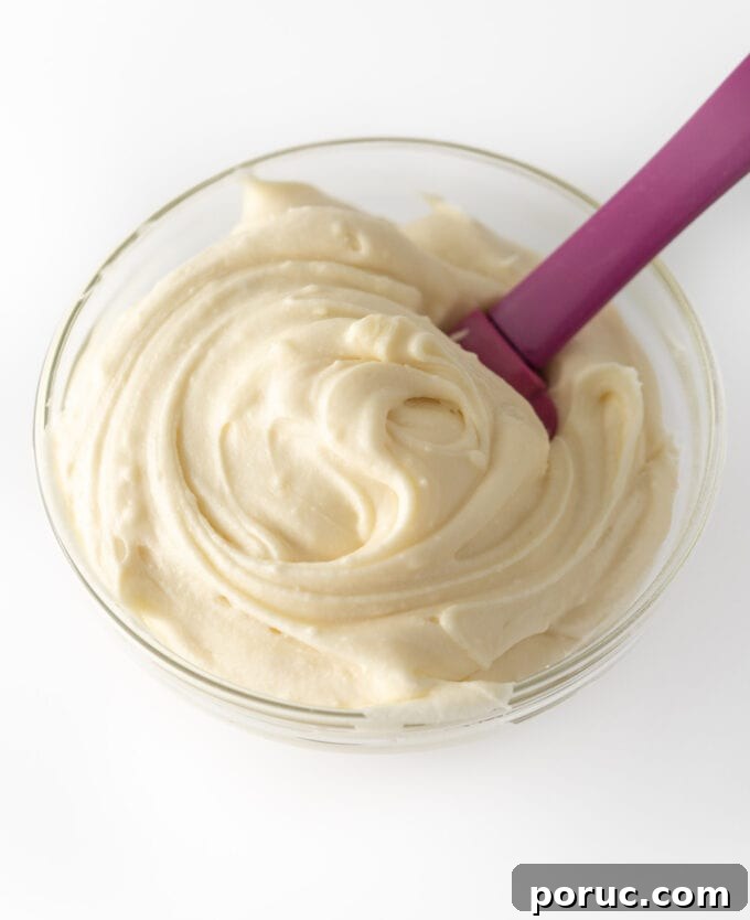 Cream Cheese Frosting Recipe for Perfect Cinnamon Rolls 3 Overhead view of fluffy cream cheese frosting in a glass bowl being stirred with a purple spatula