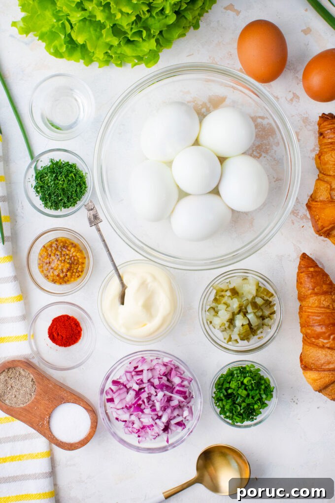 Overhead shot of classic egg salad ingredients in bowls on a white surface.