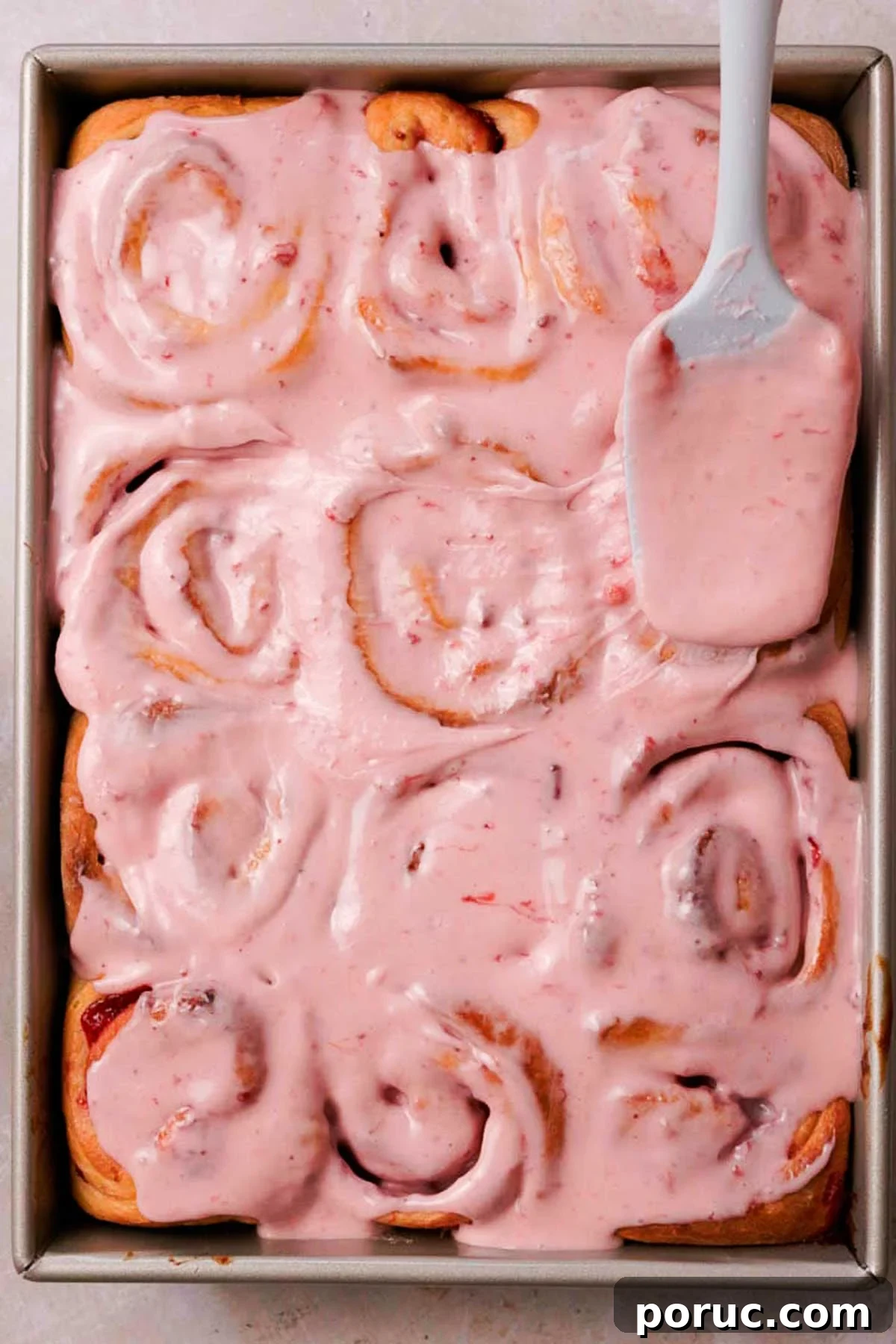 Strawberry Cinnamon Roll Recipe — Soft, Sweet, Homemade Treat 20 spreading pink glaze over baked strawberry cinnamon rolls