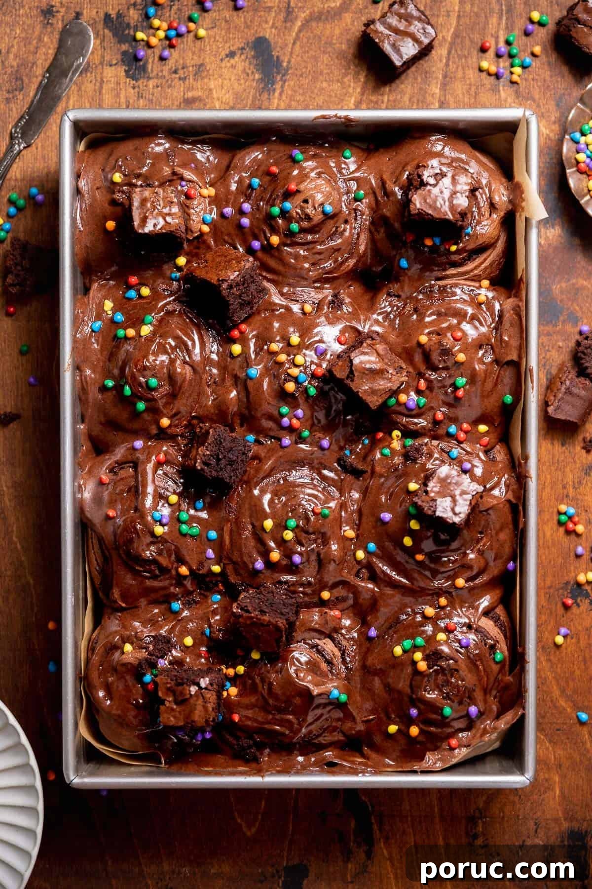 Chewy Cosmic Brownie Roll Recipe with Sprinkle Filling 2 Overhead view of frosted cosmic brownie cinnamon rolls topped with brownie pieces and rainbow candy-coated chips.