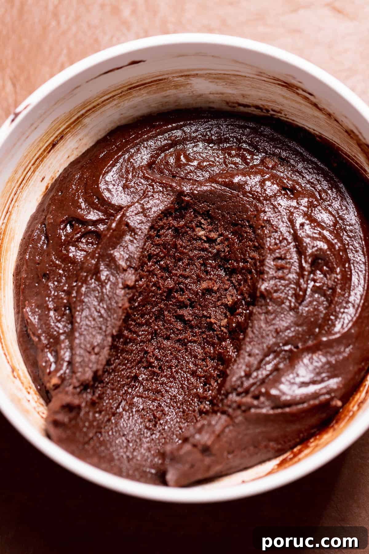 Chewy Cosmic Brownie Roll Recipe with Sprinkle Filling 5 Homemade brownie batter filling in a white bowl with a spoon scoop removed, showing its thick texture.