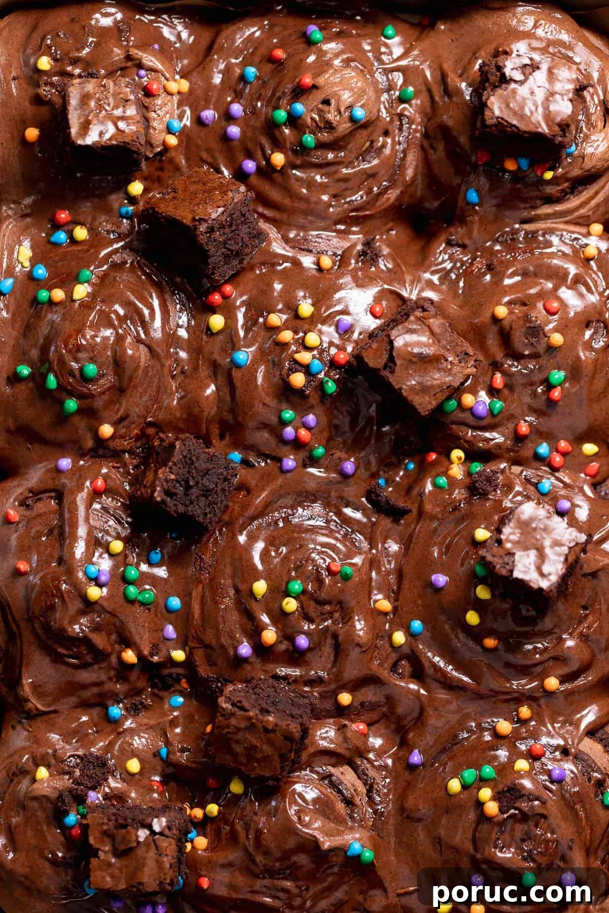Chewy Cosmic Brownie Roll Recipe with Sprinkle Filling 10 Cosmic brownie rolls topped with chocolate cream cheese frosting, fudgy brownie chunks, and rainbow candy-coated chips in a baking pan.