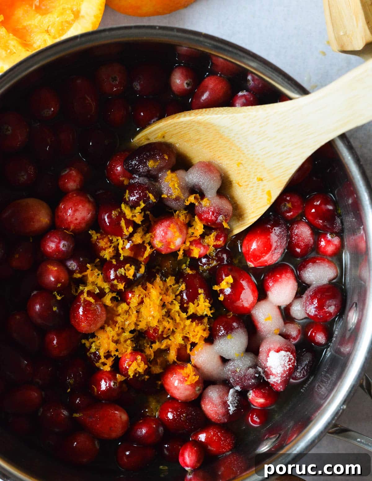 a pot with cranberries, sugar, orange zest, and apple cider in it. 