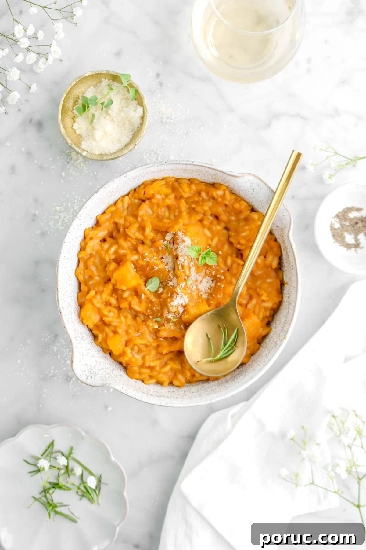Creamy Roasted Butternut Squash Risotto Recipe 2 butternut squash risotto in bowl with gold spoon on top, a bowl of grated cheese beside, a glass of wine, and white napkin.