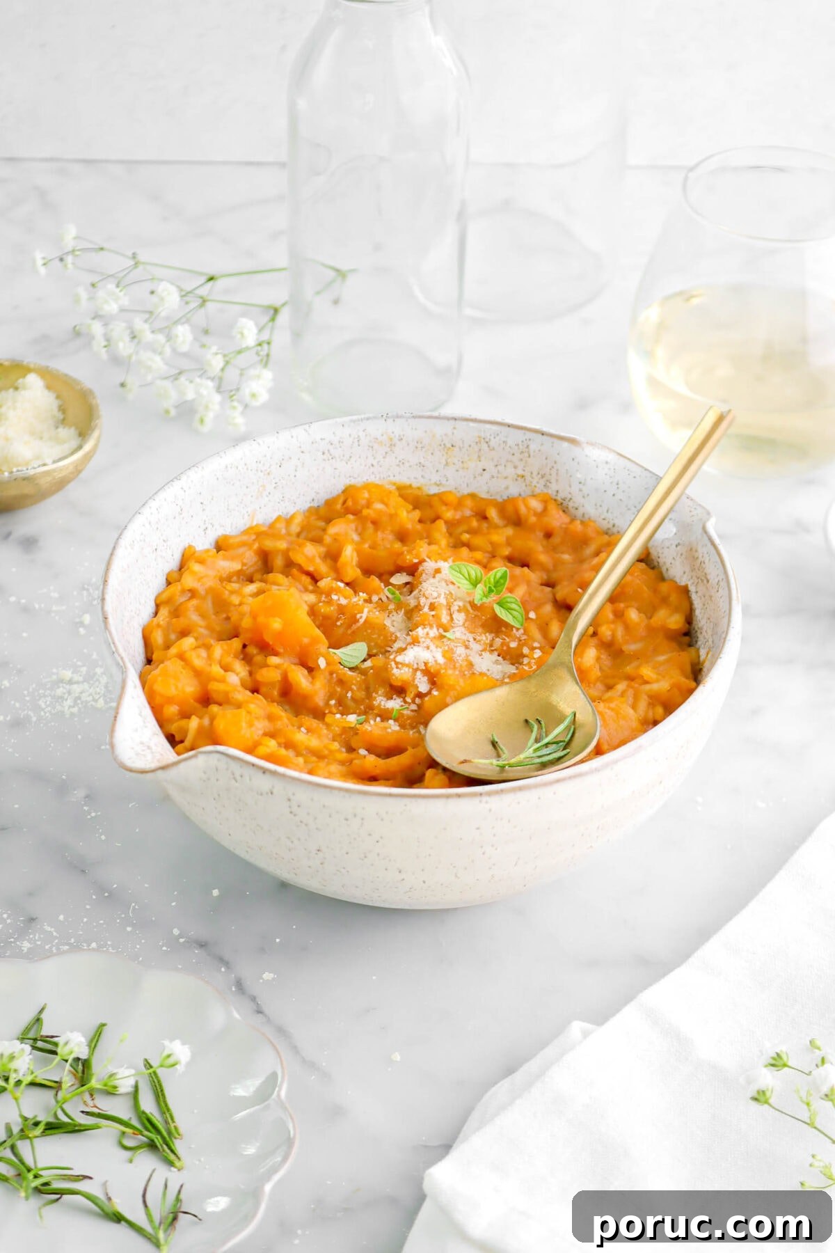 Creamy Roasted Butternut Squash Risotto Recipe 10 front shot of butternut squash risotto in large bowl with gold spoon on top, with glass of wine behind.