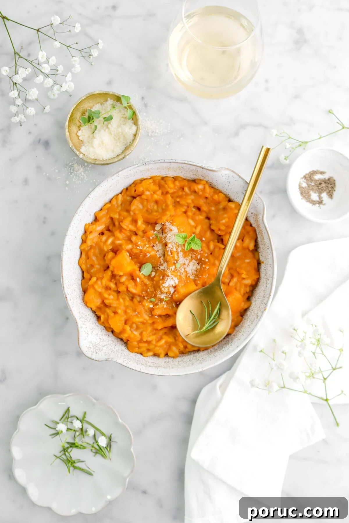 Creamy Roasted Butternut Squash Risotto Recipe 3 butternut squash risotto with cheese, oregano, gold spoon with rosemary sprig on top with white napkin and glass of wine beside.