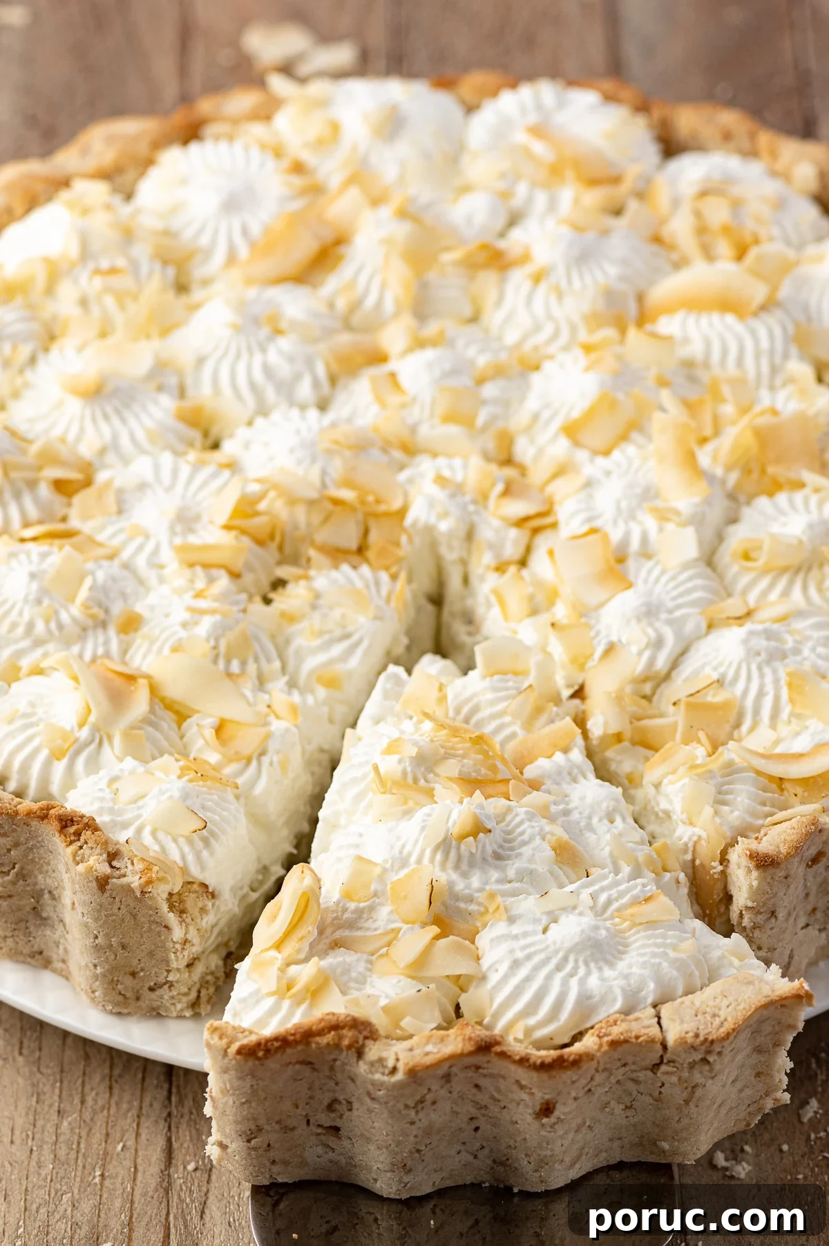 Coconut cream pie with a slice being removed on a rustic wooden table.