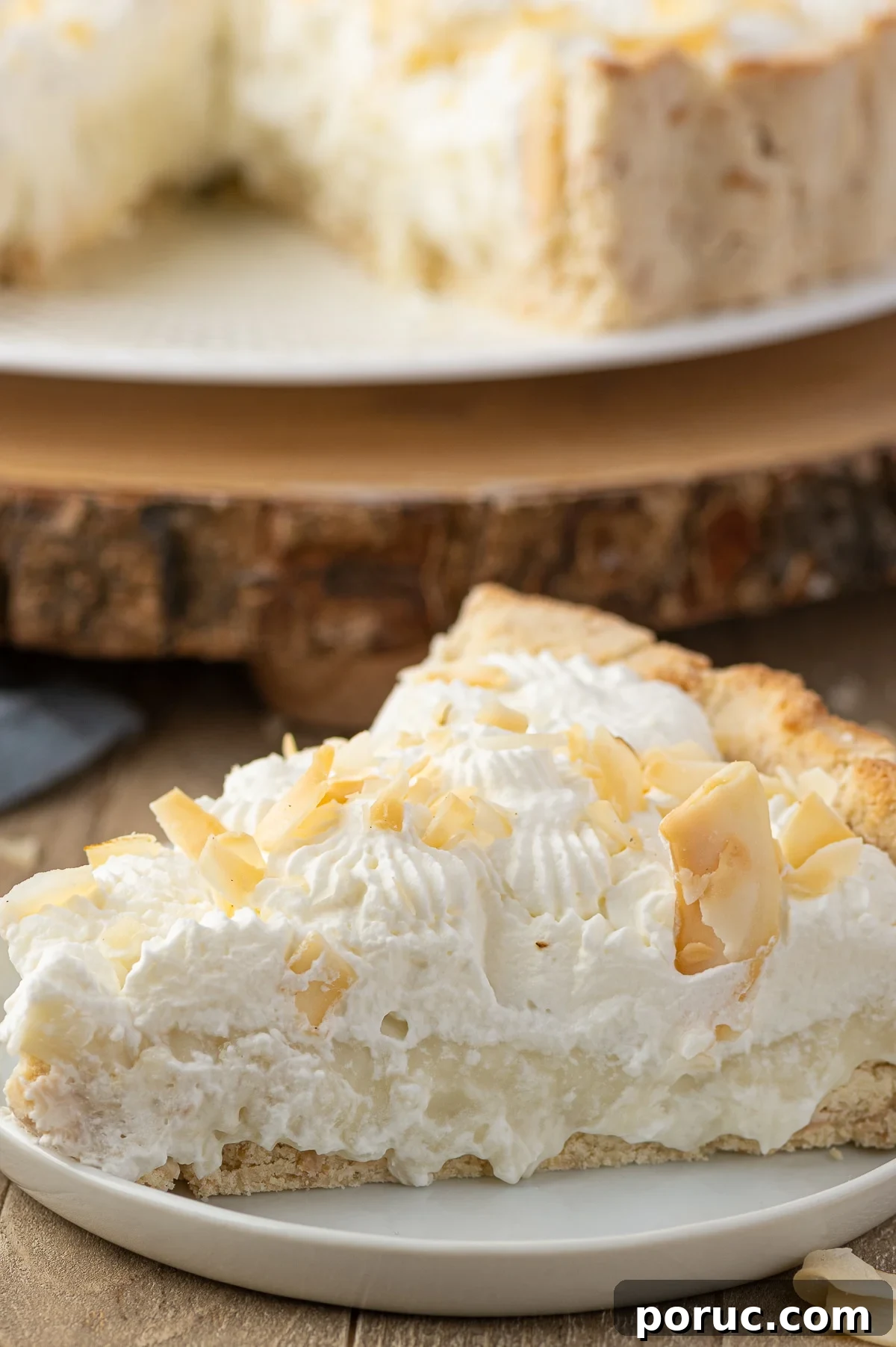 A close up photograph of a single slice of keto coconut cream pie with whipped cream topping and large toasted coconut flakes.